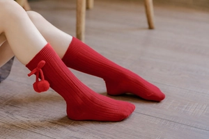 Detail of red ribbed knit baby knee high socks featuring a cute plush pom pom and bow