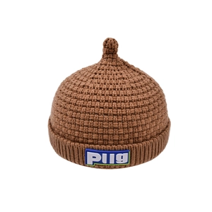 Detail of a brown knitted baby pacifier hat with a blue PUG label on the folded brim