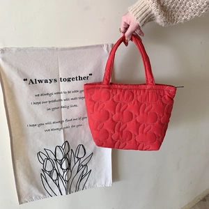 Detail of red quilted rabbit handbag held by hand against a minimalist fabric backdrop