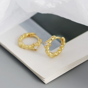Macro shot of gold twist rope hoop earrings featuring a single square zircon inlay