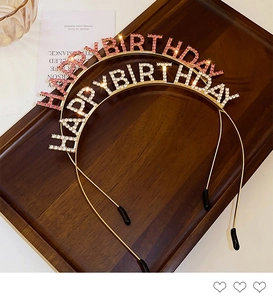 Detail view of pink and white crystal Happy Birthday headbands on a wooden tray