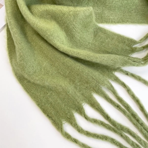 Close-up of light green mohair scarf with soft fuzzy texture and braided fringe detail