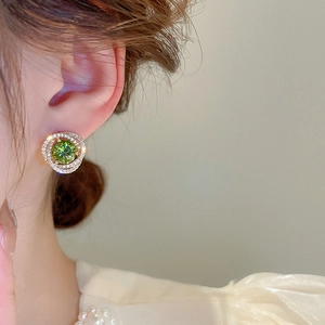 Detail of model wearing gold earrings with a green stone and shimmering zircon accents