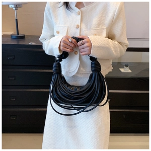 Detail of black pleated shoulder bag with unique coiled handle held by model in white suit