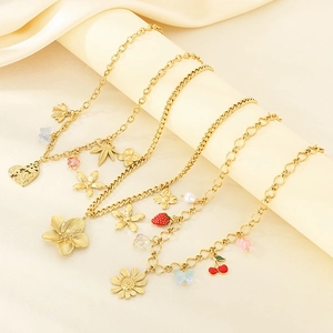 Three gold chain necklaces with heart, leaf, and cherry charms on fabric display