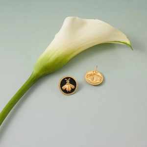 Détail de boucles d'oreilles abeille en acier doré 18K et émail noir sur une fleur blanche