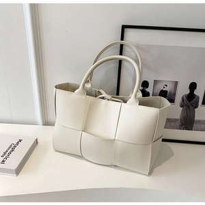 Detailed close-up of woven cream tote bag showing square pattern and texture on white surface