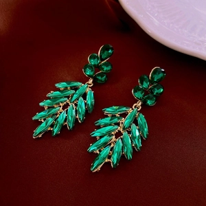 Macro detail of leaf-shaped earrings with green crystals on a red velvet surface