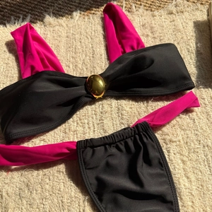 Flat lay detail of a black three-piece bikini with pink ties and a golden metal ring buckle