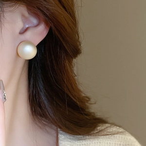 Close-up of a matte gold geometric round stud earring worn by a model for a chic look