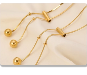 Macro detail of 18K gold plated hollow ball pendant and sleek tassel chain necklace