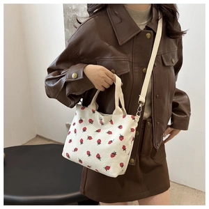Detail of white corduroy shoulder bag featuring a vibrant red strawberry print pattern