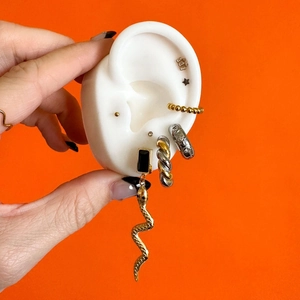 Golden stainless steel earring set featuring snake drops and studs on a silicone ear model