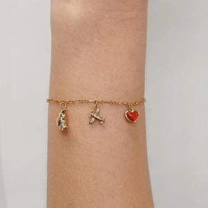 Close-up of gold chain bracelet with croissant, airplane, and red heart charms on wrist