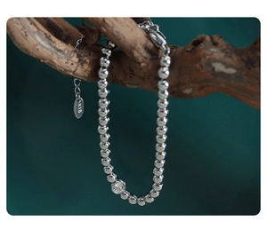 Macro detail of silver beaded bracelet with K18 gold tag and zircon on a wooden branch