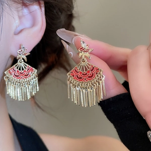 Detail of gold fan tassel earrings with red enamel and clear zircon stones on a model