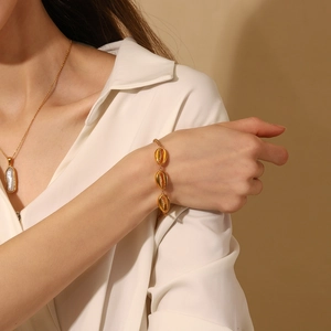 Detailansicht der 18K vergoldeten Muschelanhänger an einem schicken Gliederkettenarmband
