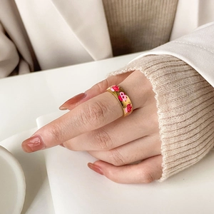Close-up of a gold ring with pink enamel heart patterns worn by a model in soft light