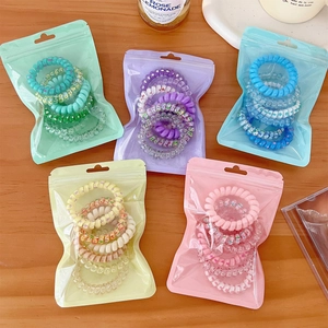 Detail of colorful gradient spiral hair ties in matte resealable bags on a wooden desk
