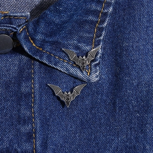 Close-up of black and silver metal bat enamel pins styled on a dark blue denim jacket collar