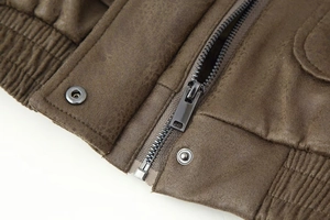 Detail view of brown leather jacket with metal zipper, buttons and ribbed hem