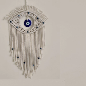 Detailed view of handmade beige cotton tapestry with blue evil eye beads and tassels