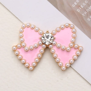 Elegant pink enamel bow charm with pearl border and central crystal on ivory background
