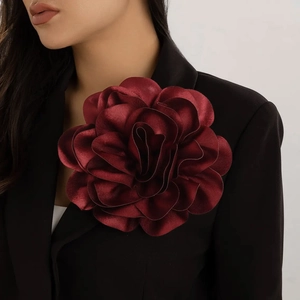 Detail of a large burgundy satin rose brooch pinned on a black tailored blazer jacket