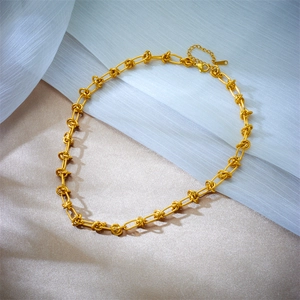 Detailed shot of golden knot link chain necklace on white silk and beige fabric