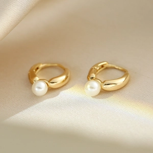 Macro shot of gold hoop earrings with white pearls on a soft beige silk fabric