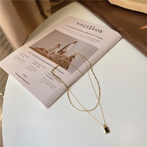Detail view of double-layered gold necklace with black rectangular pendant on Vogue magazine