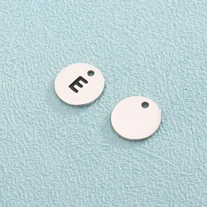 Polished titanium steel round pendant charms with hollow letter E on blue background