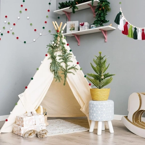 Detail of a beige canvas teepee tent with festive green wreaths and colorful pompoms