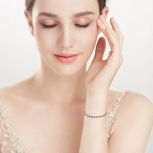 Detail of silver tennis bracelet featuring red and white zircons on model's wrist