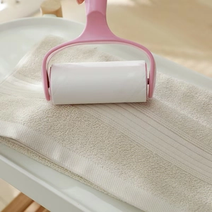 Pink lint roller removing hair from soft cotton towel on a minimalist wooden table