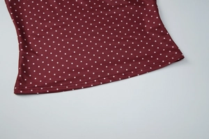 Dettaglio del tessuto bordeaux a pois con cucitura dell'orlo a doppio ago e texture definita
