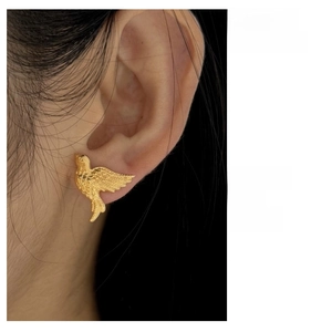 Close-up of golden swallow stud earrings with feather details worn by a model