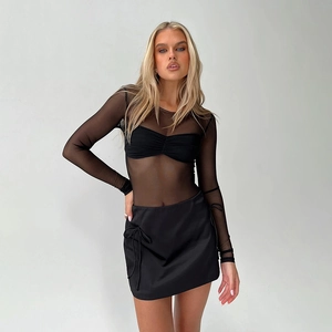 Detail of sheer black mesh long-sleeve top and satin mini skirt with bow detail