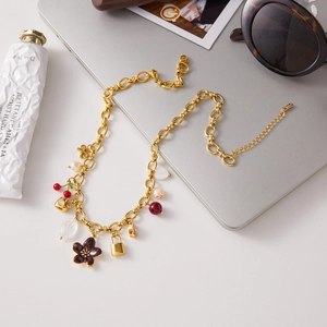 Flat lay of a gold charm necklace with red flowers, pearls, and cherry pendants on a desk