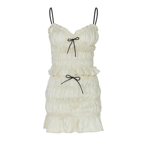 Detail of white pleated chiffon dress featuring elegant black bow accents and ruffled hem