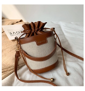 Detail of canvas and leather bucket bag with drawstring closure on a soft fabric base
