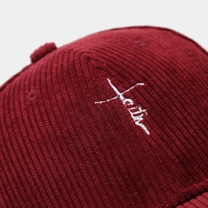 Détail macro de casquette de baseball en velours bordeaux avec broderie cursive blanche