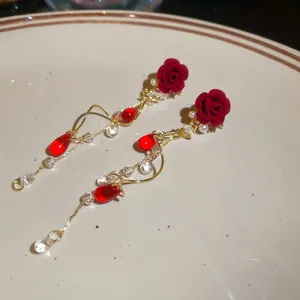 Elegante Ohrringe mit roten beflockten Rosen, Goldquasten und Perlen auf weißem Porzellan