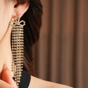 Dettaglio di orecchini a fiocco dorati con lunghe nappe di strass su una modella