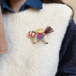 Detail of embroidered horse brooch with golden sycee and fabric texture on a sweater