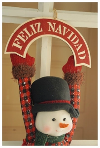 Close-up of a plush snowman ornament holding a red banner with Feliz Navidad greeting