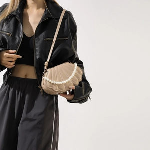 Chic beige shell-shaped crossbody bag with pearl chain detail worn on person