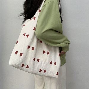 Detail of a large beige canvas tote bag with red heart pattern worn by a model