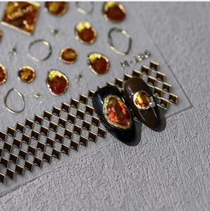 Macro detail of amber nail gems and gold lattice stickers on dark display tips