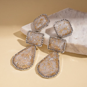 Détail de boucles d'oreilles géométriques en résine avec feuilles d'or et argent